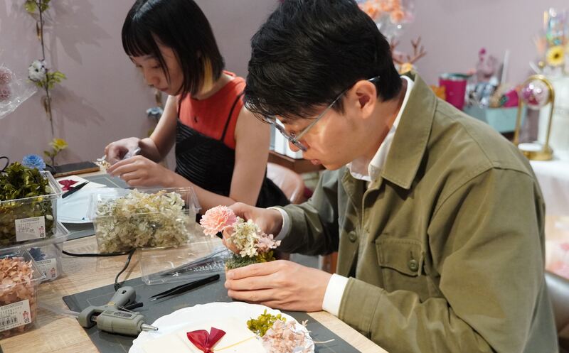 圖:高市青年局長林楷軒(右)在花藝師的指導下,手作母親節花禮要向媽媽表達謝意